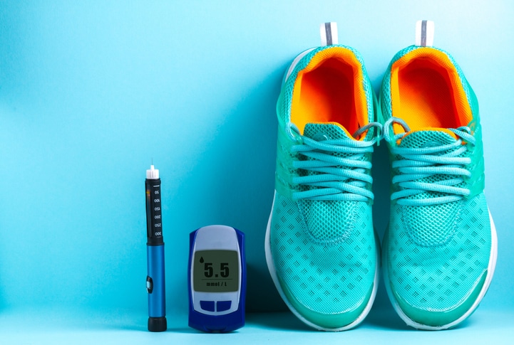 A pair of teal sneakers next to a dark blue diabetic blood sugar monitoring device and a lancet on a light blue background.