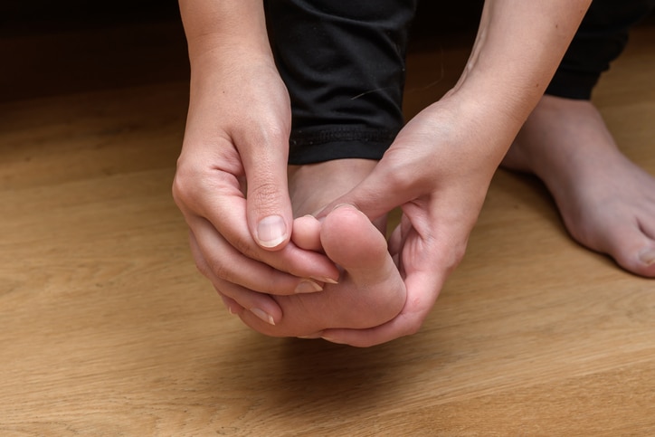 A person holds and examines their foot, focused on their big toe.