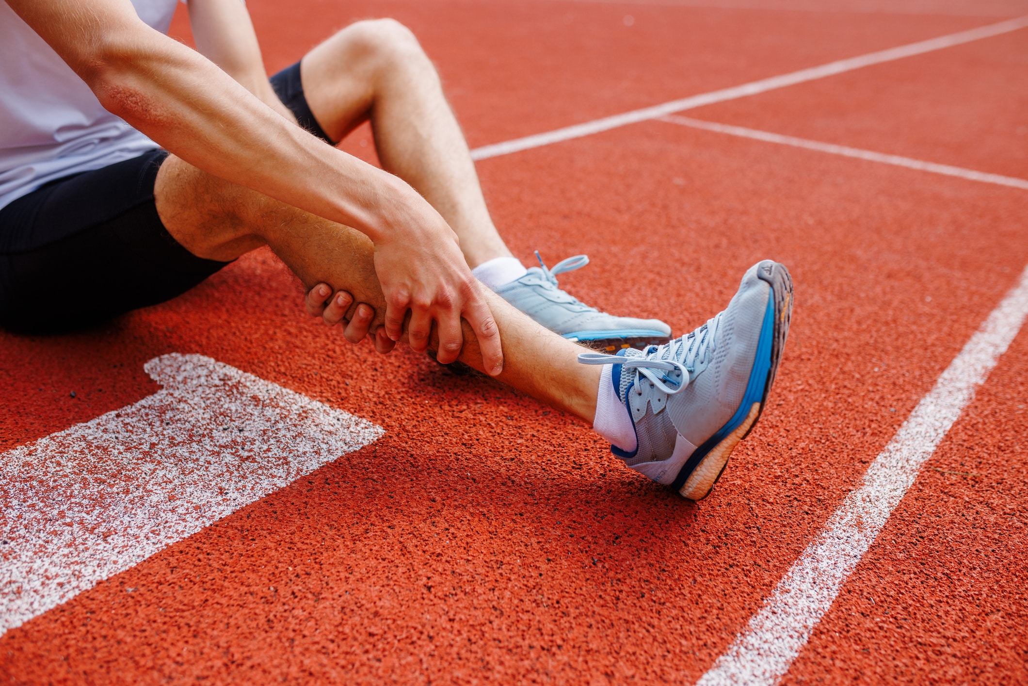A runner on the ground holding his calf after a painful sports injury.