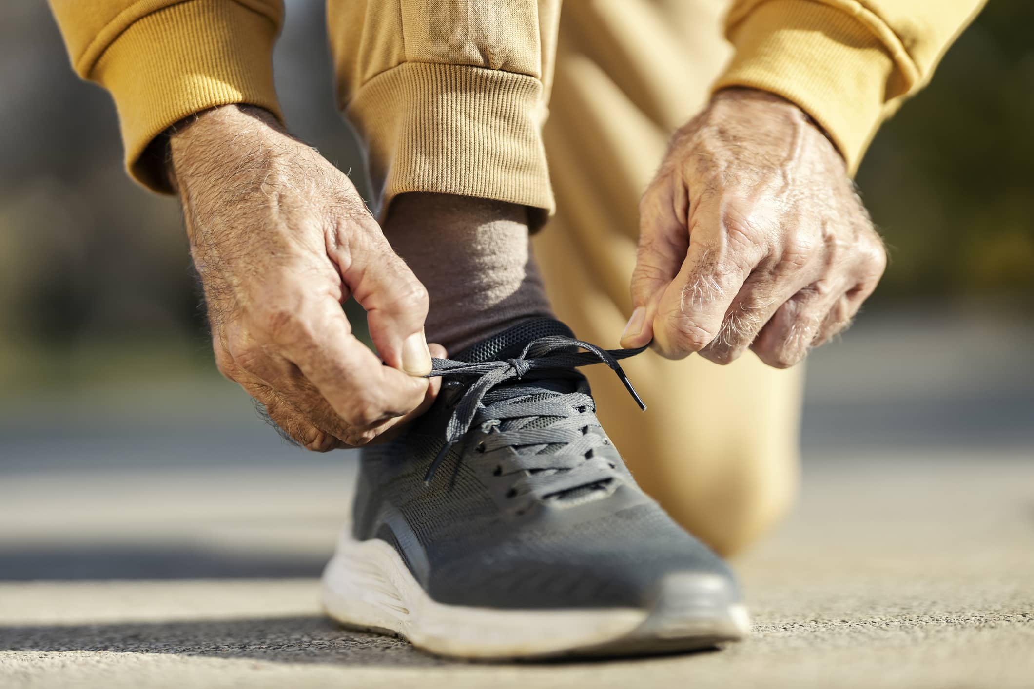 An elderly man in a yellow tracksuit tying his shoe for an active workout.