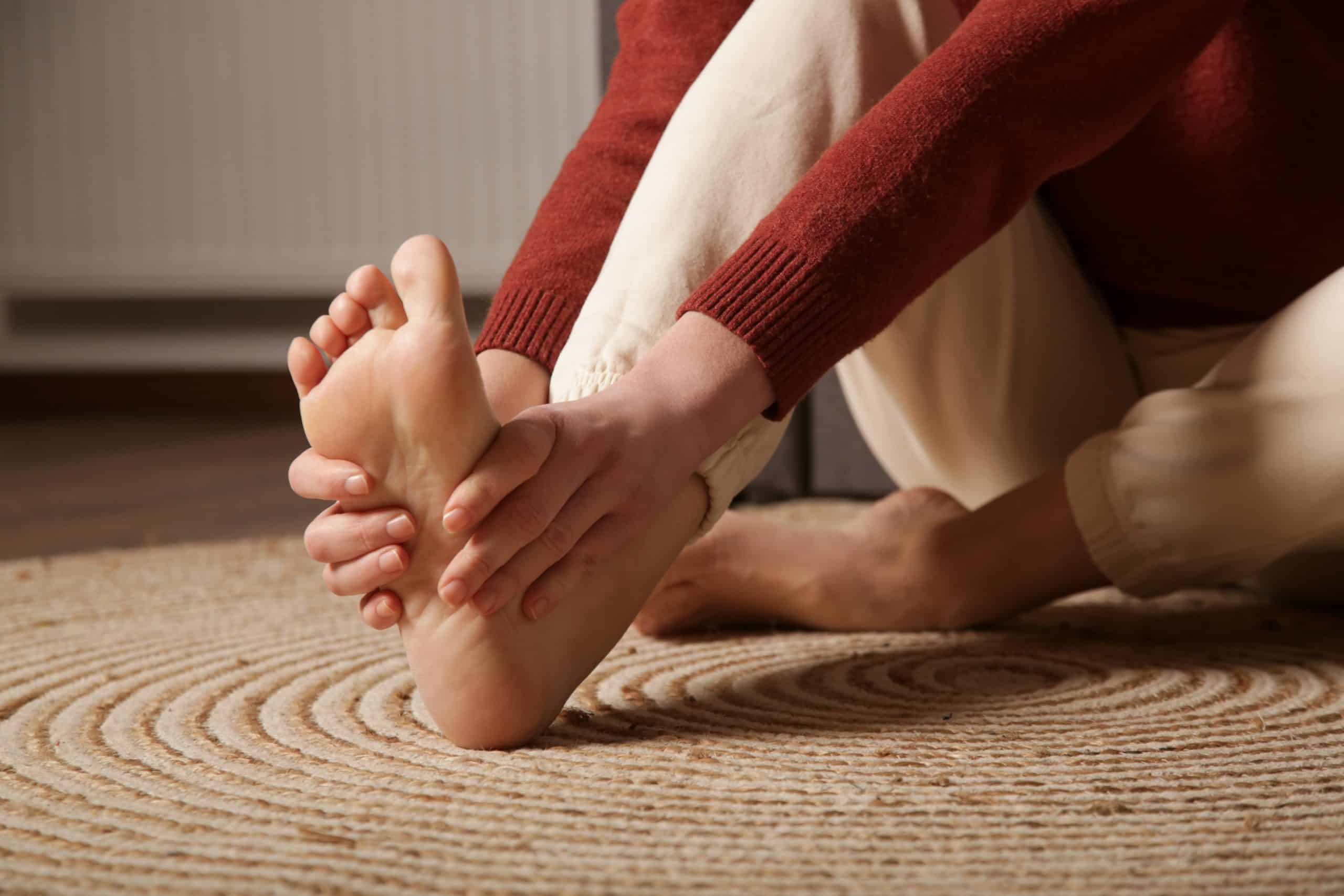 Person sitting and rubbing the bottom of their foot, showing discomfort from numbness or tingling in the feet.