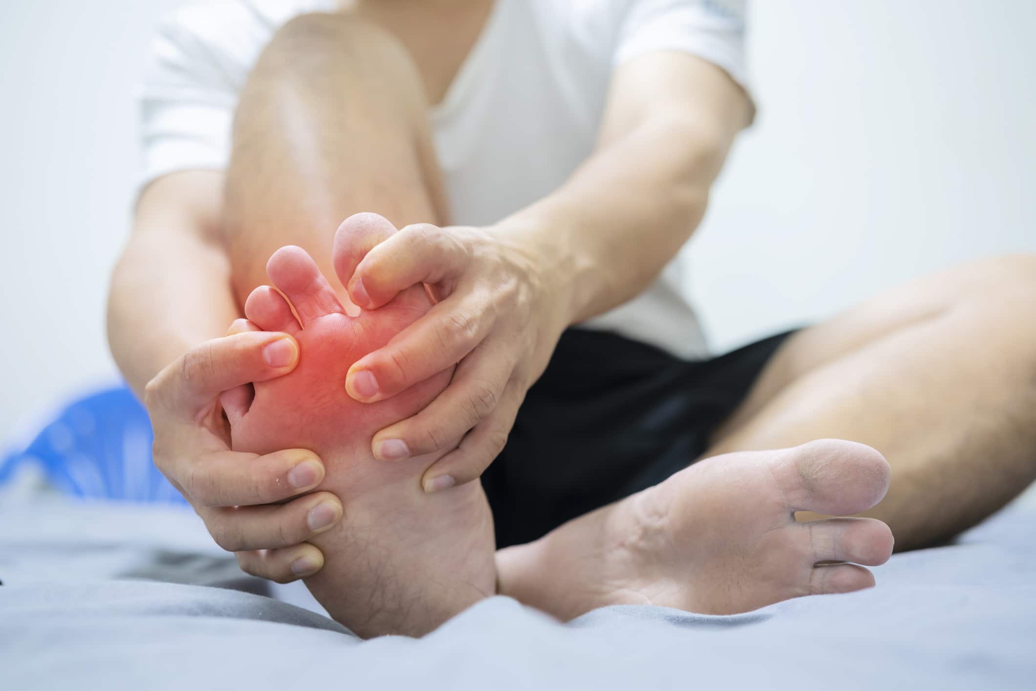 Person holding the ball of their foot in pain while sitting, showing discomfort from metatarsalgia or forefoot pressure.